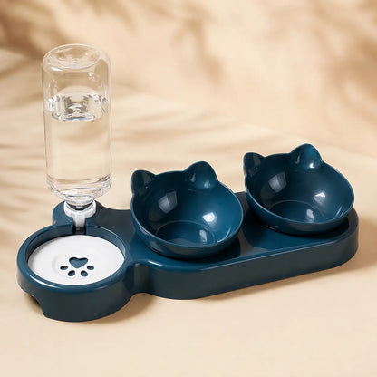 A pet water fountain and double bowl set in dark teal, featuring two cat-shaped bowls, a clear water bottle, and a white paw-print filled dish on a beige background.