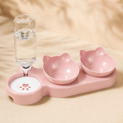 Pink pet feeding station with two cat-ear bowls, a water bottle holder, and a paw-print water dish on a beige fabric background.
